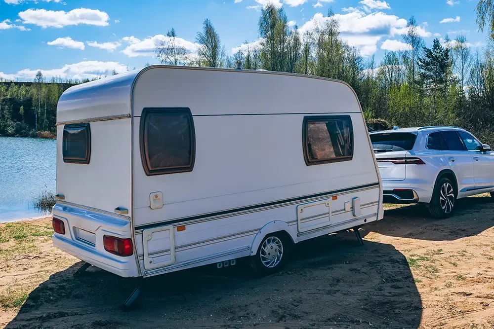 White trailer parked by serene lake, with SUV nearby, suited for road trips and outdoor adventures featuring high performance trailer tires and SUV tires. 